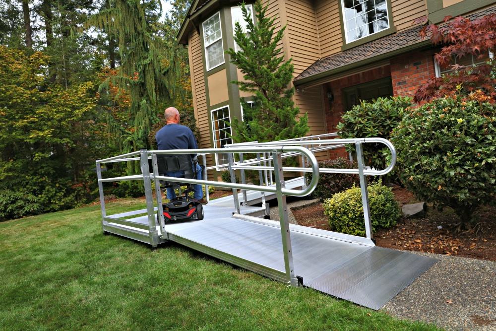 man riding power chair up aluminum ramp to the front door entrance of his home