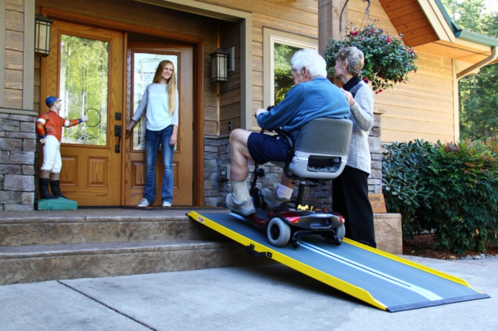 elderly man in scooter using portable ramp to access front door of a house