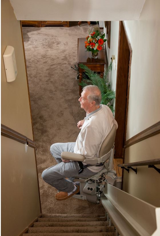 man riding curved stair lift in his home to safely access the bedroom upstairs