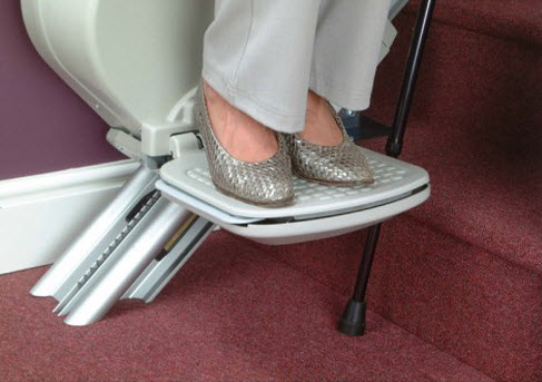 stair lift track at bottom landing with woman riding chair and feet on footrest